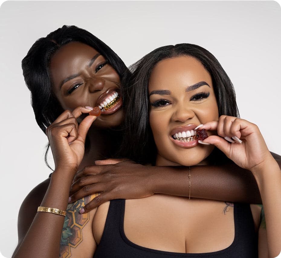 Two women smiling and biting gummy vitamins together.
